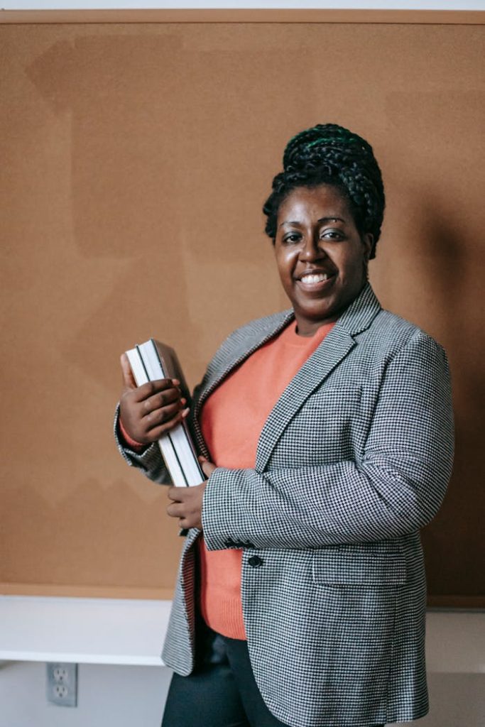 Smiling black teacher with books in classroom